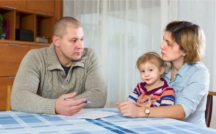 a married couple with a child at a table filling out paperwork