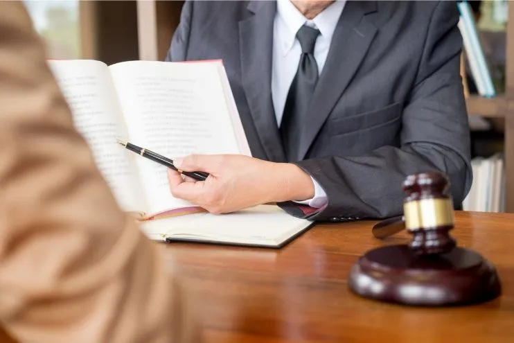 attorney pointing a pen at a book next to gavel
